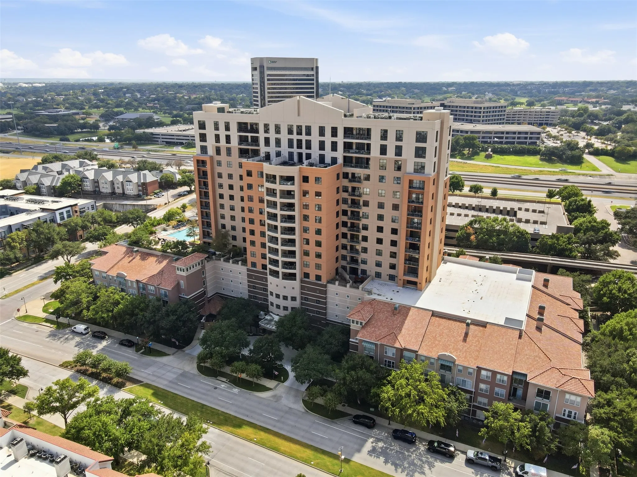 High-rise building with multiple balconies, a ground-level swimming pool, and surrounding mature trees