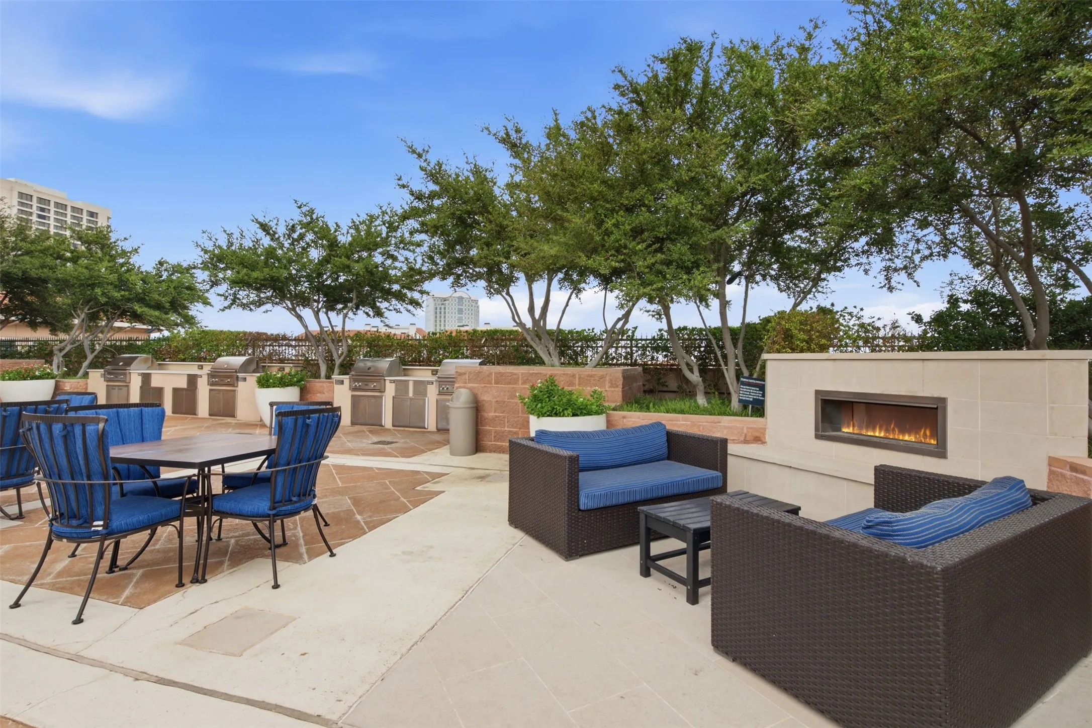 Expansive outdoor patio featuring multiple built-in grilling stations, a gas fireplace, and mature trees