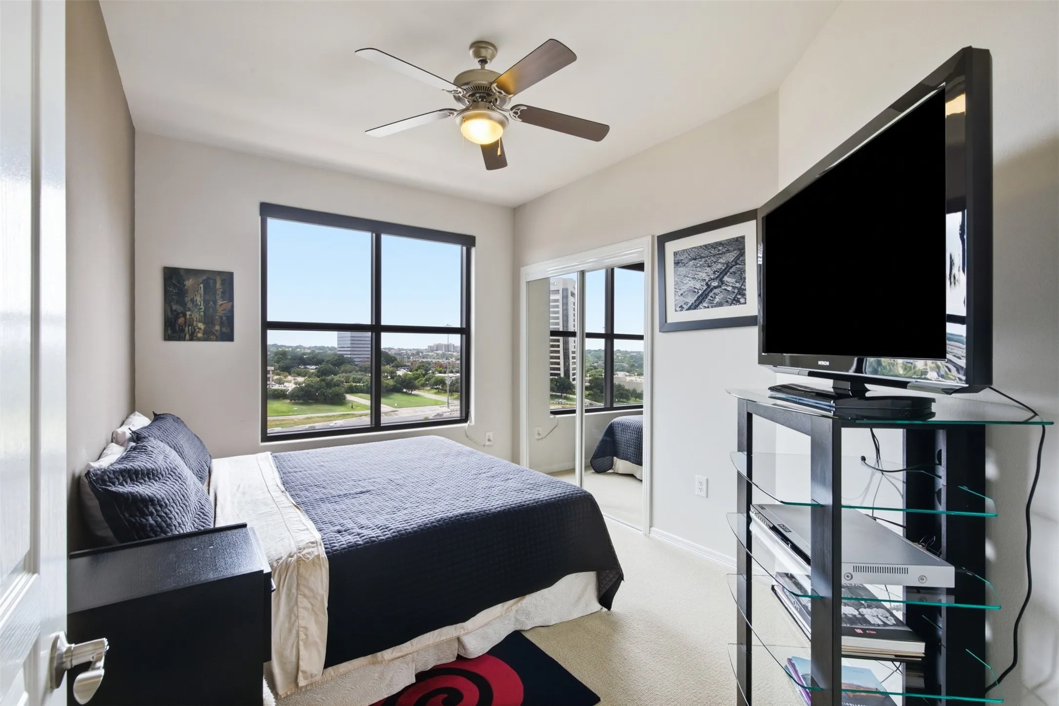 Large window with exterior scenery, ceiling fan with integrated lighting, mirrored sliding closet doors, and carpeted flooring