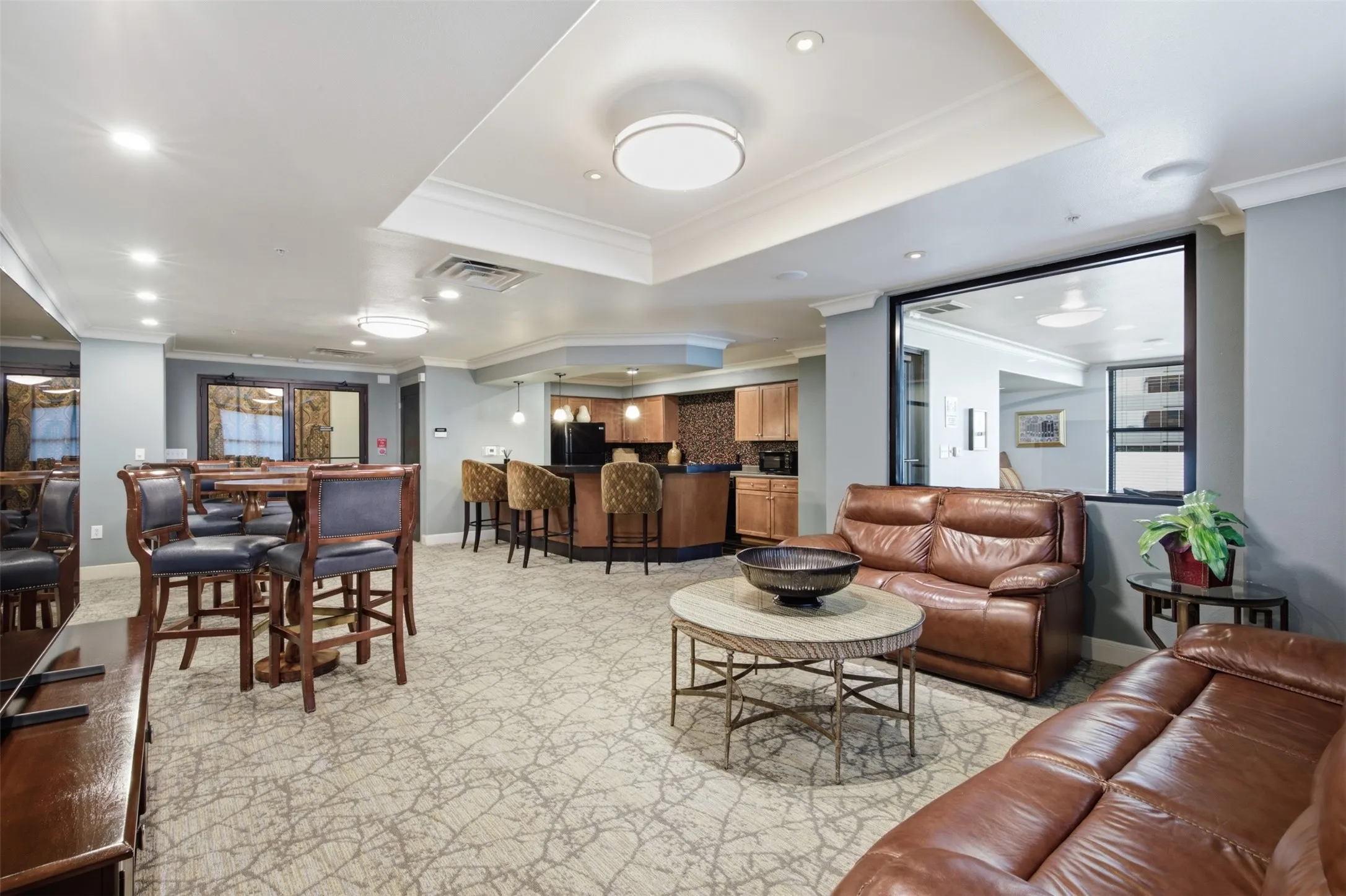 Spacious common area featuring patterned carpeting, recessed lighting, and a built-in bar with pendant lighting