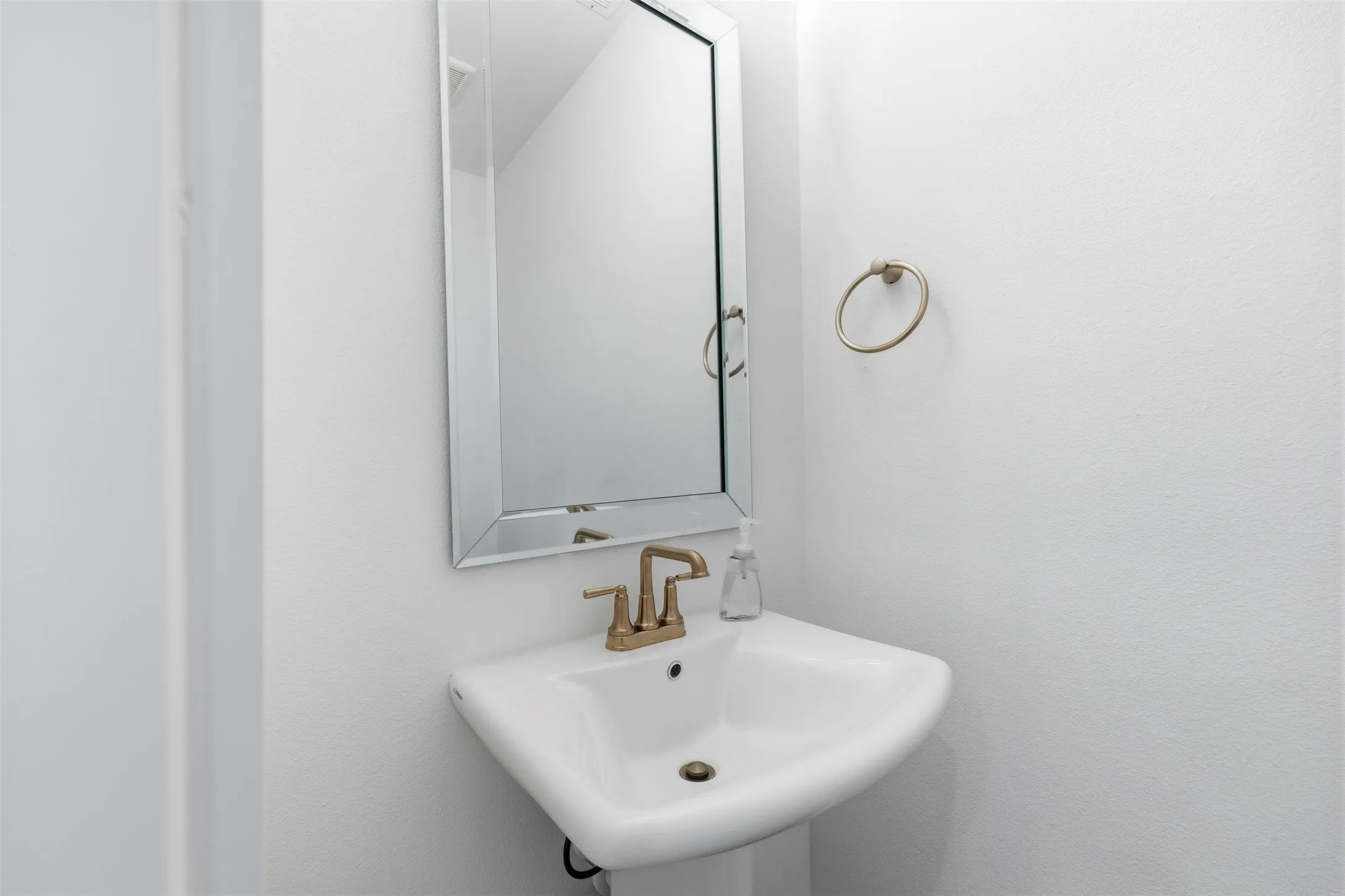 Pedestal sink with a gold-tone faucet, complemented by a rectangular framed mirror and a gold-tone towel ring