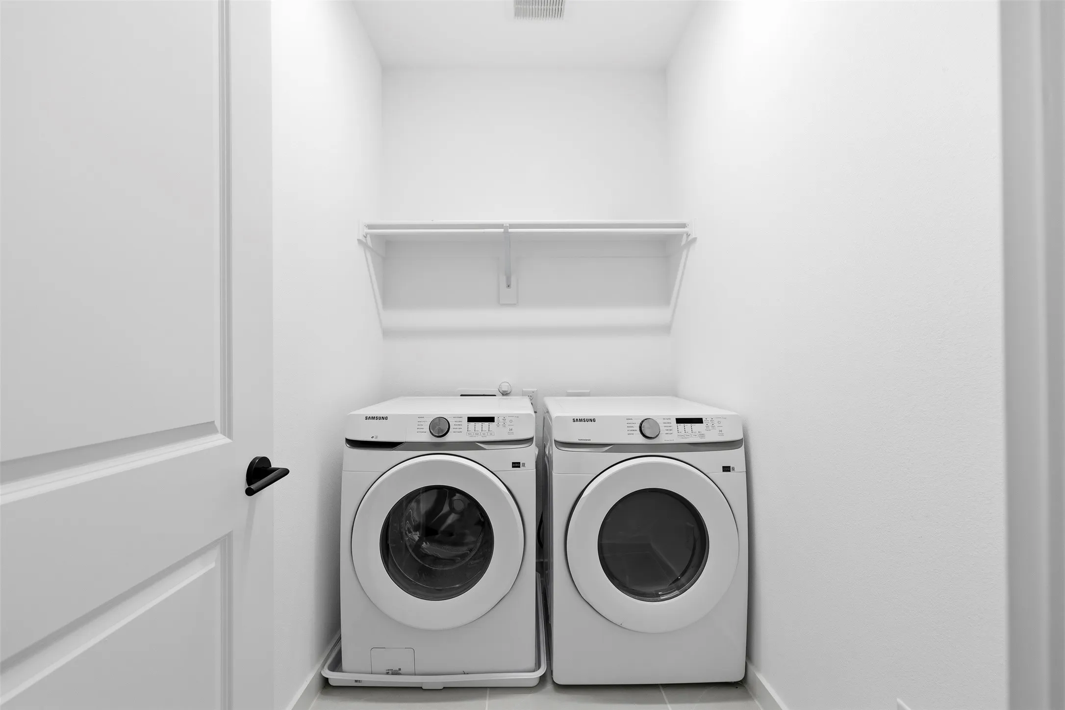 Dedicated laundry area featuring a white storage shelf and modern front-load appliances