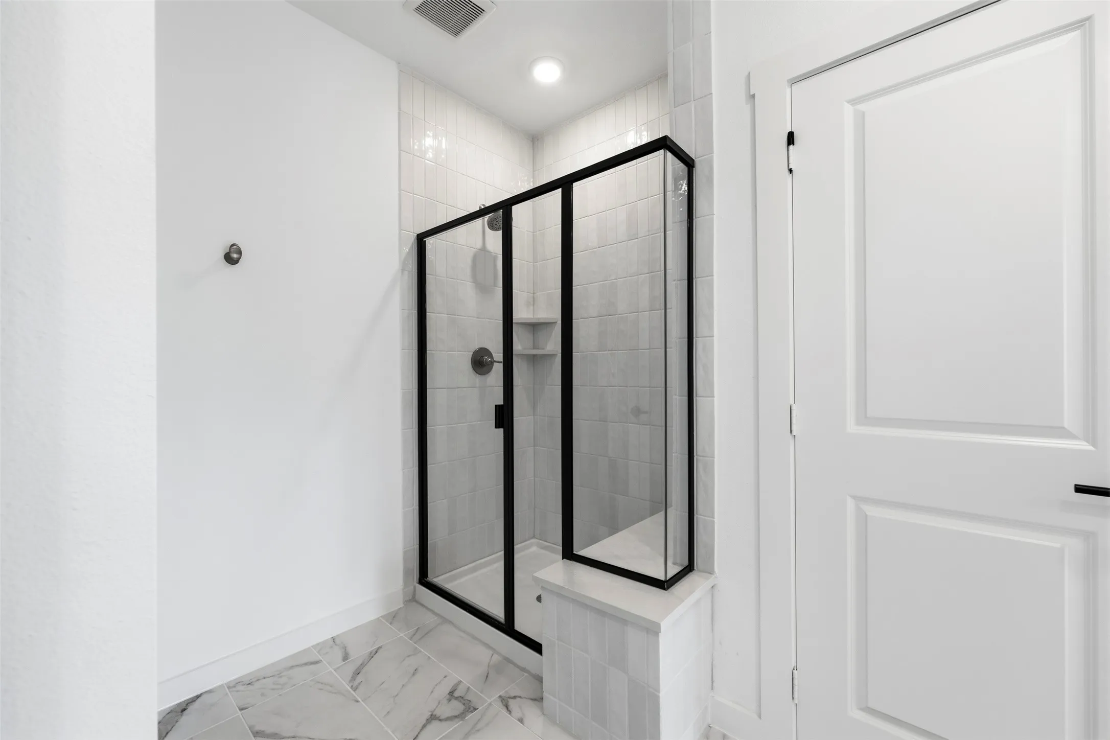Shower enclosure with black framing, tiled walls, built-in shelf, and a built-in bench