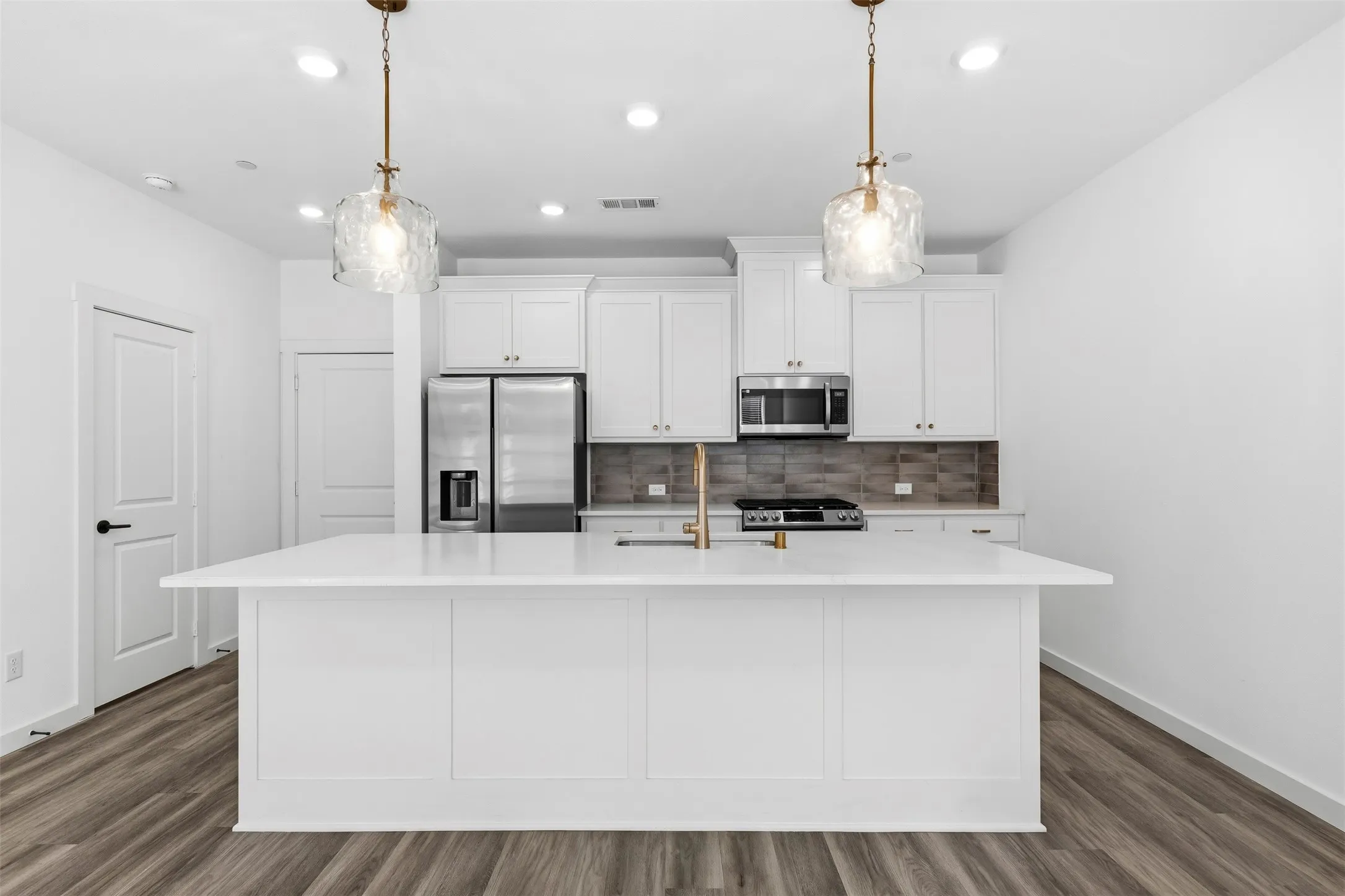 Central island with a solid surface countertop, white cabinetry, stainless steel appliances, and wood-finish flooring