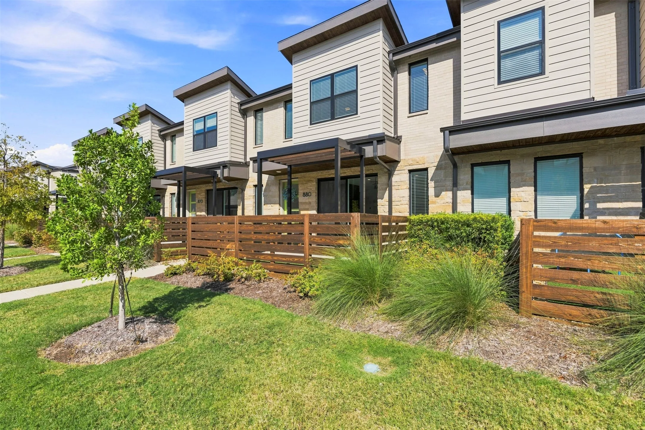 Contemporary townhome exterior featuring stone and siding finishes, individual patios with pergolas, and a horizontal slatted privacy fence
