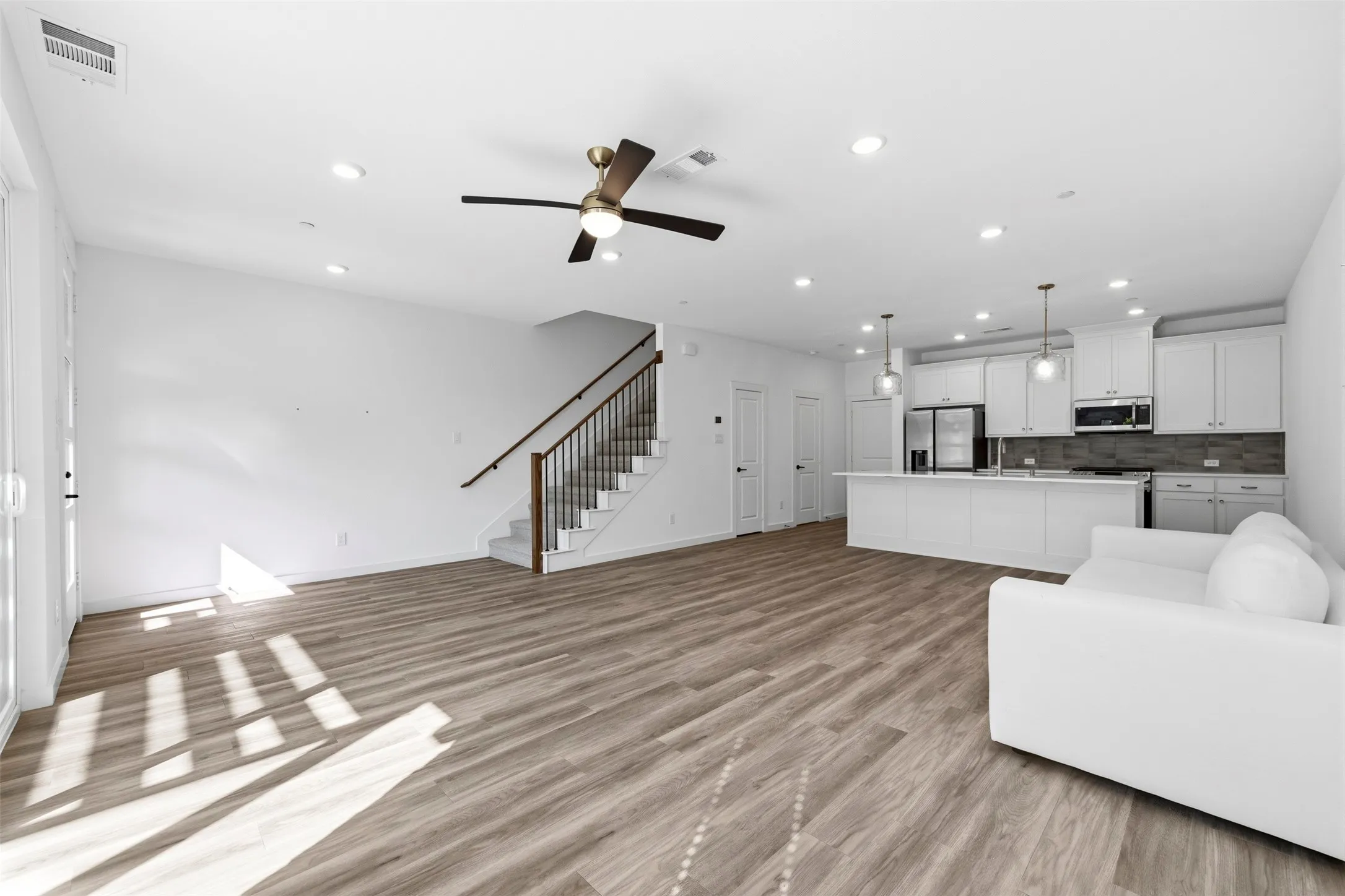 Open-concept living area featuring wood-finish flooring, recessed lighting, a modern ceiling fan, and a staircase with metal balusters