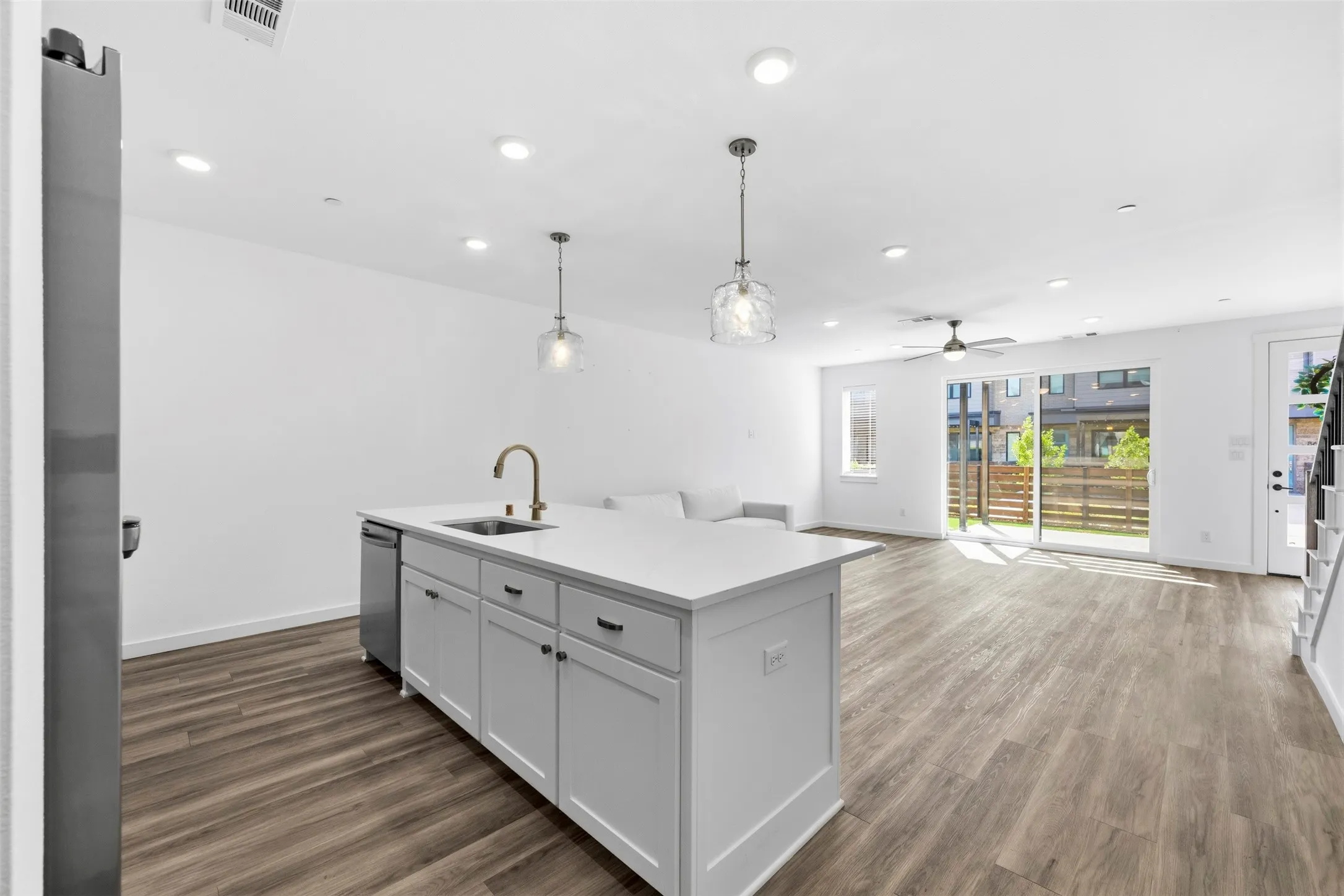 Open concept living space featuring wood-finish flooring, white cabinetry, a kitchen island with integrated sink, and recessed lighting