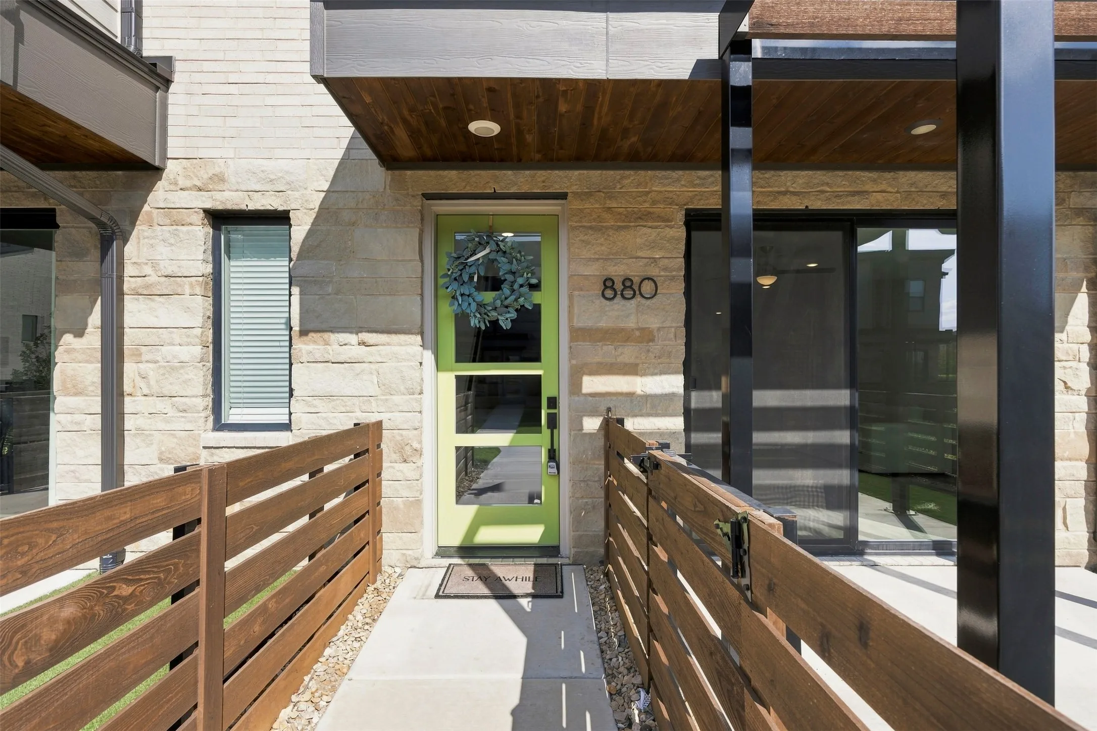Stone facade with a vibrant entry door, featuring a concrete walkway and wood-finish fencing