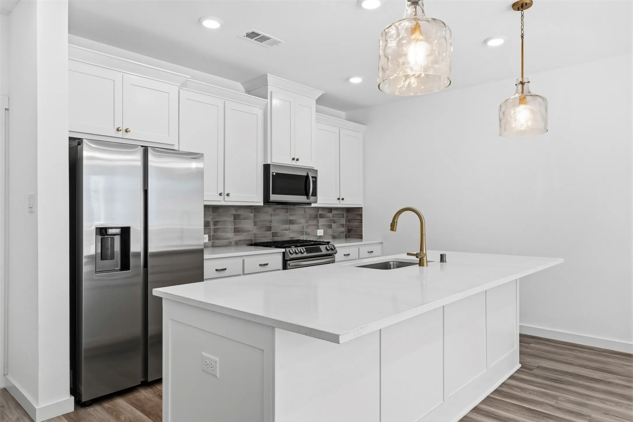 White shaker-style cabinetry, stainless steel appliances, a center island with a sink, white countertops, and wood-finish flooring