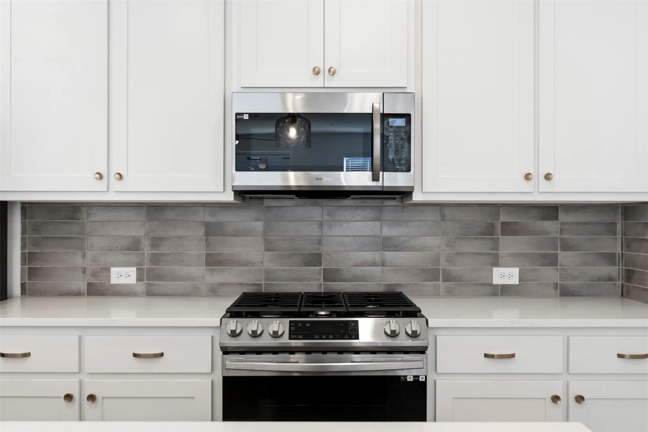 White cabinetry, stainless steel microwave, stainless steel range, white countertops, and gray subway tile backsplash