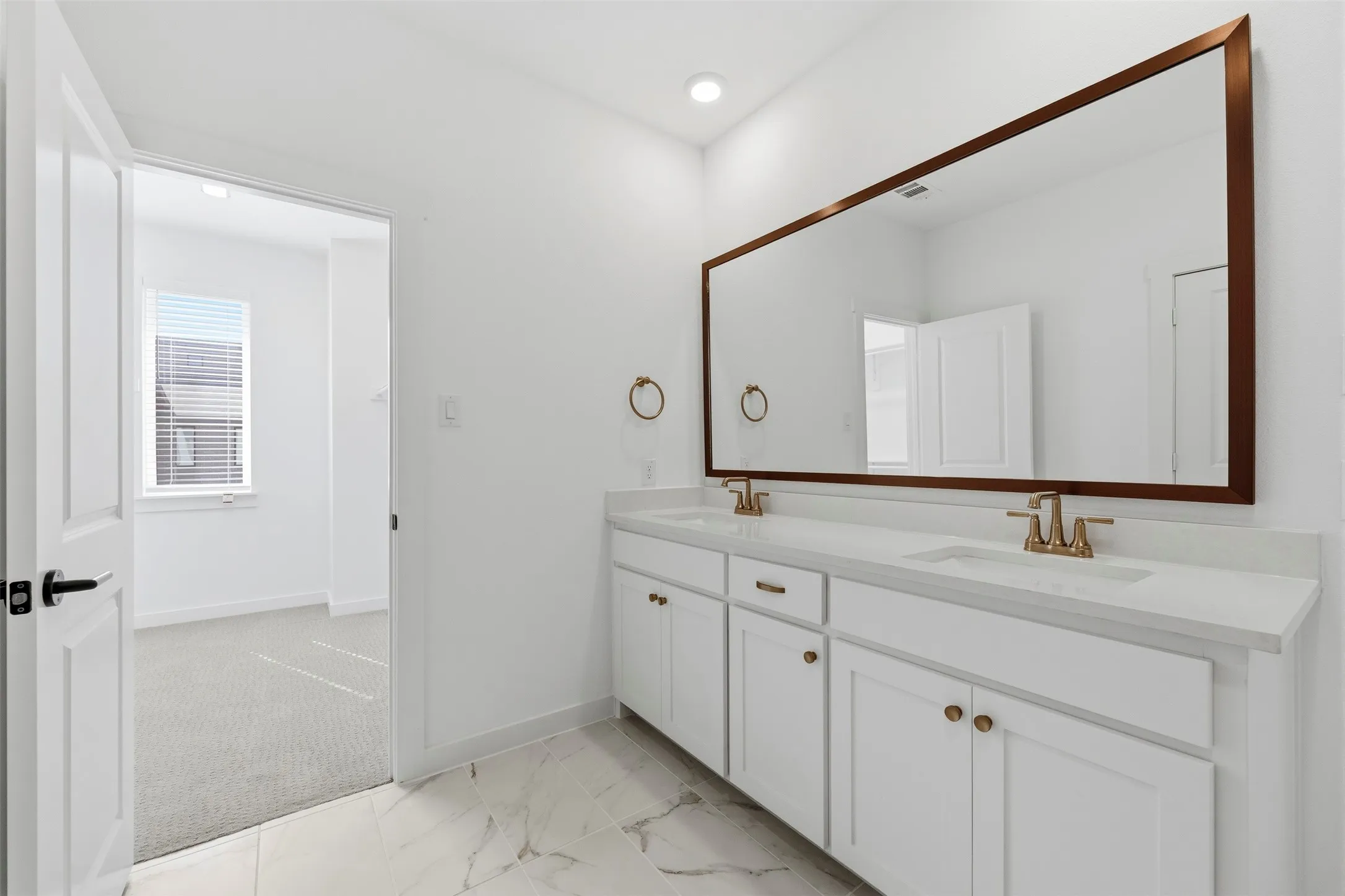 Dual vanity with white cabinetry and gold-tone hardware, white countertop, and a large framed mirror