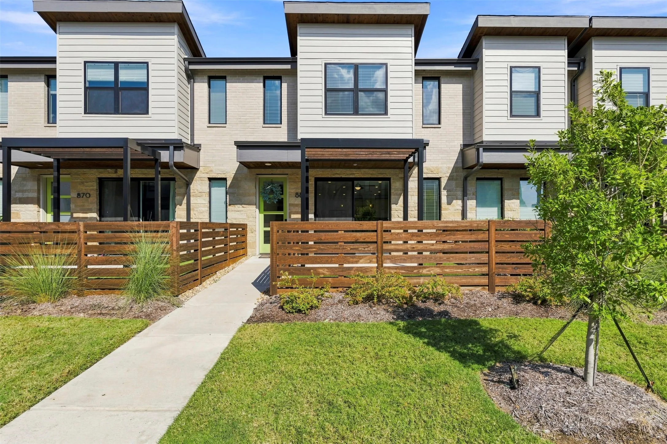 Modern townhome exterior with mixed material siding, flat roofline, private front patio with wood fencing, and concrete walkway