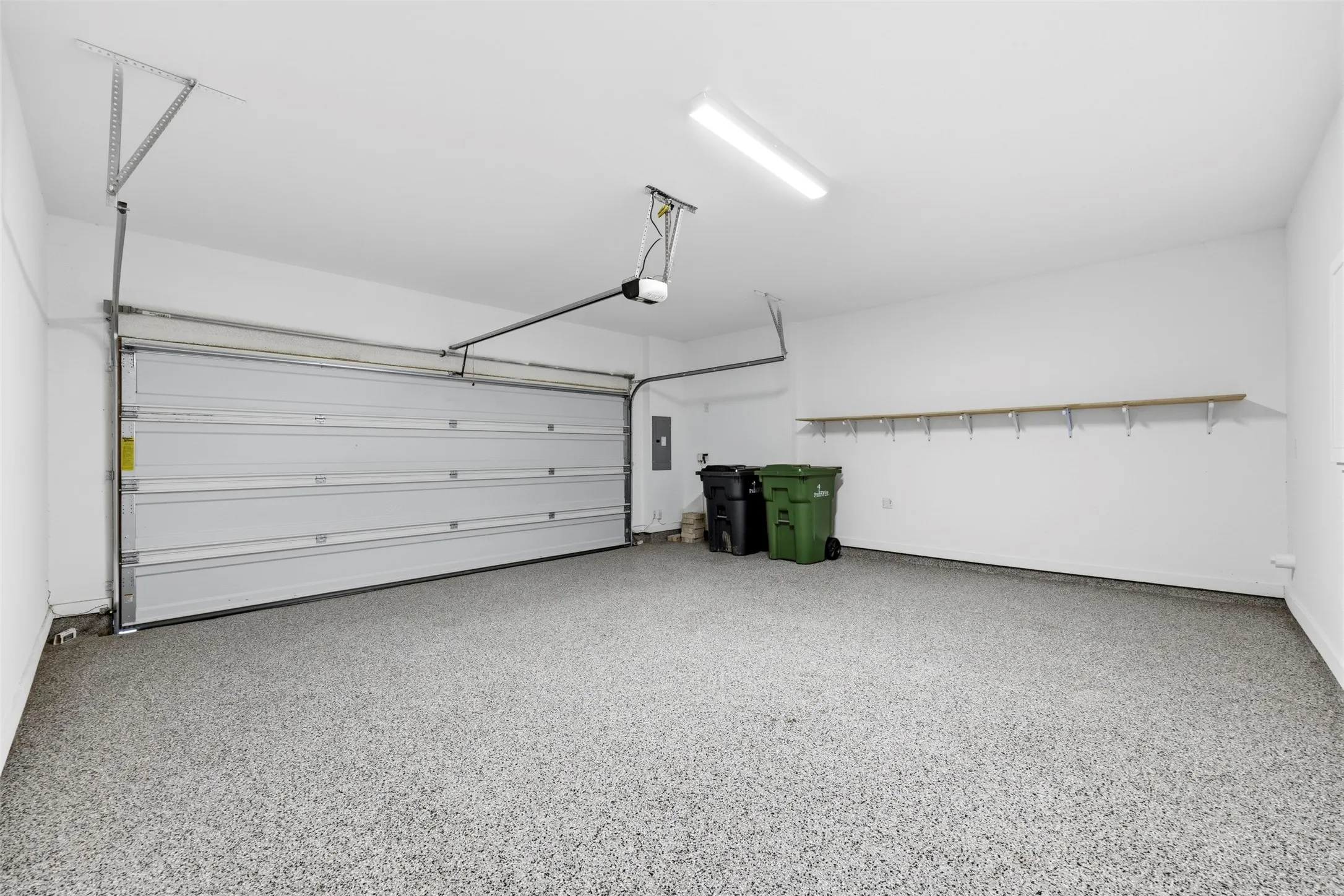 Two-car garage featuring an automatic garage door, epoxy flooring, built-in wall shelving, and overhead lighting