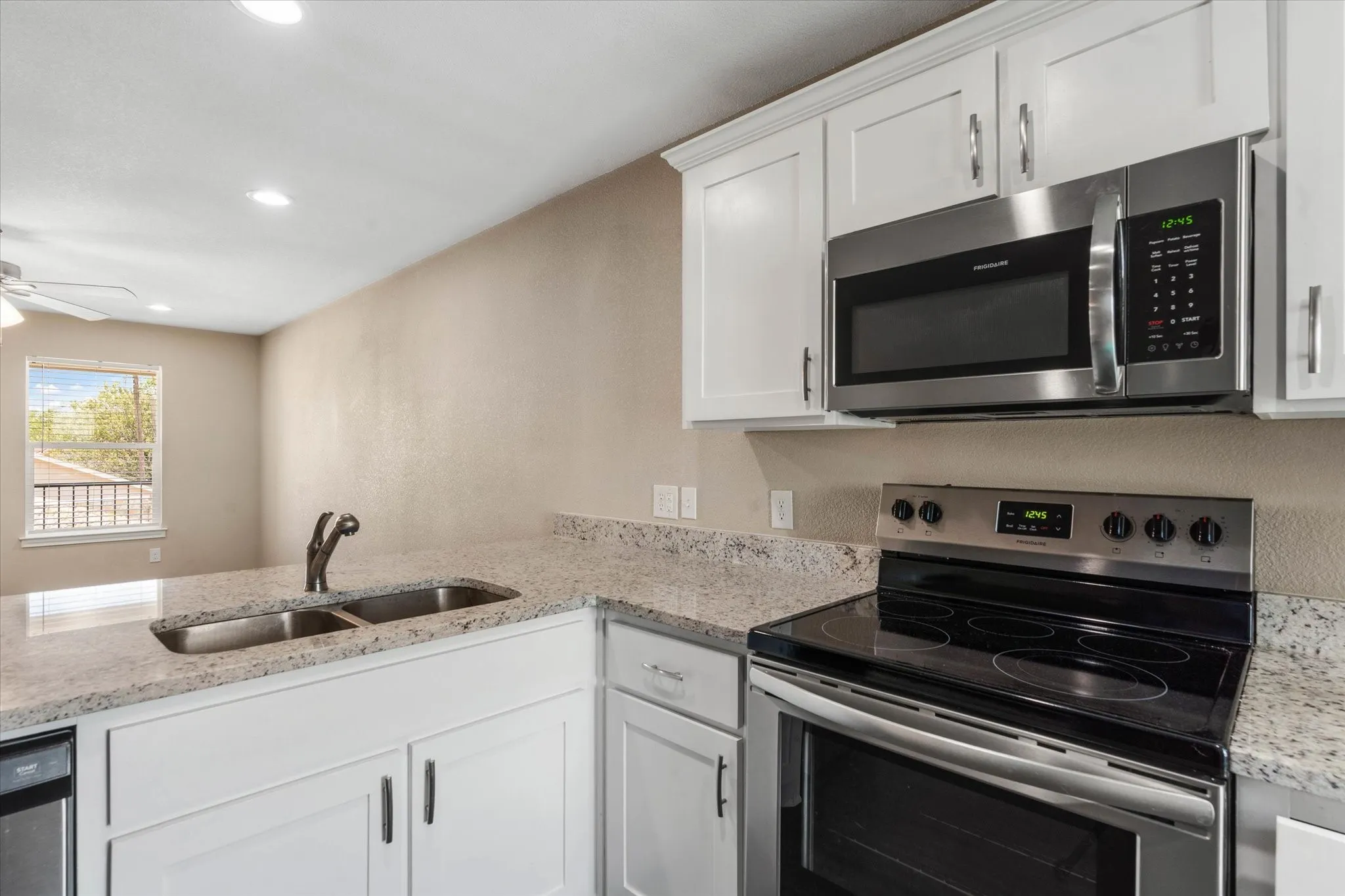 Kitchen with stainless steel appliances, white cabinets, sink, light stone counters, and ceiling fan