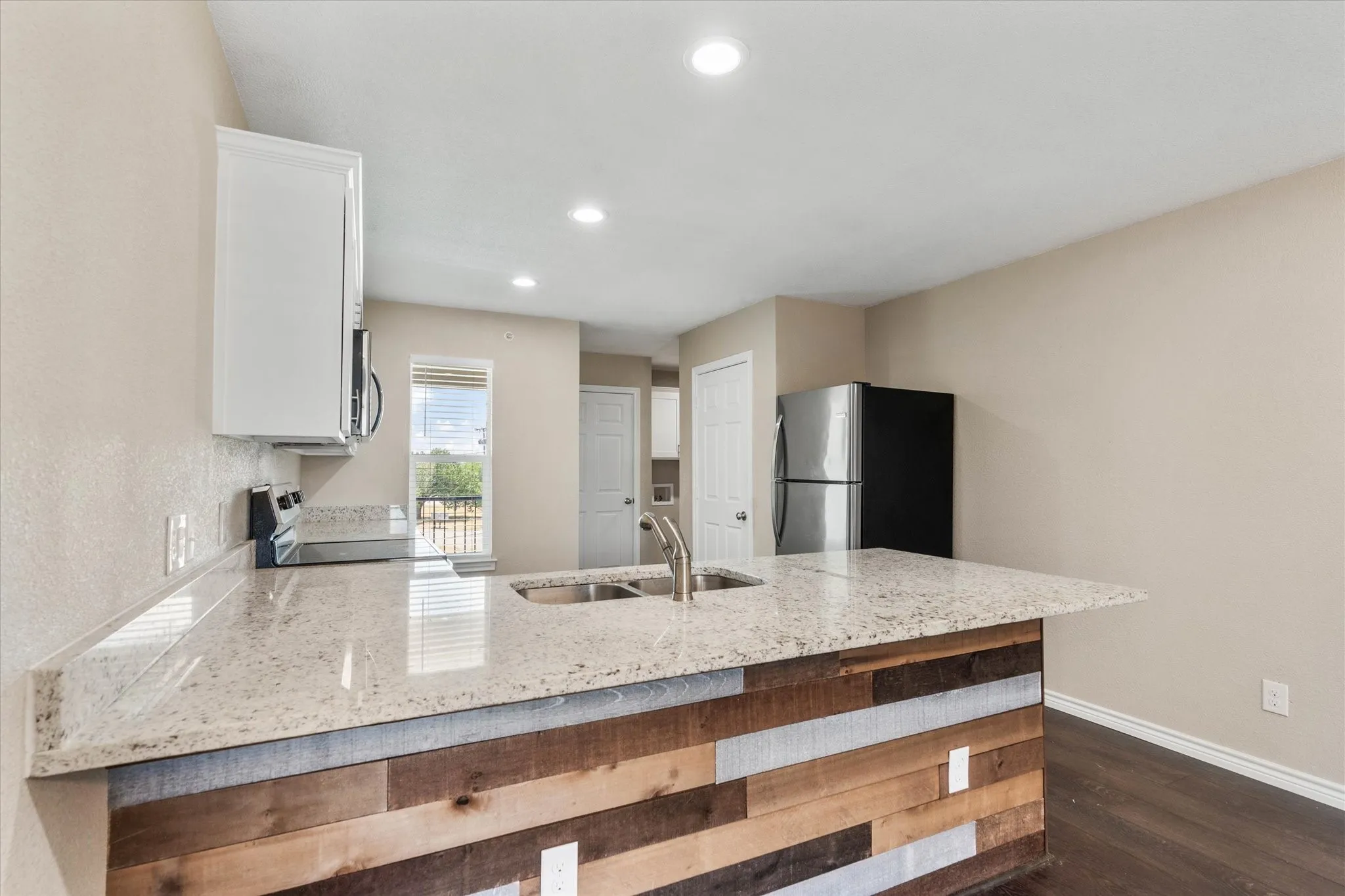 Kitchen with white cabinetry, kitchen peninsula, dark hardwood / wood-style floors, stainless steel appliances, and light stone countertops