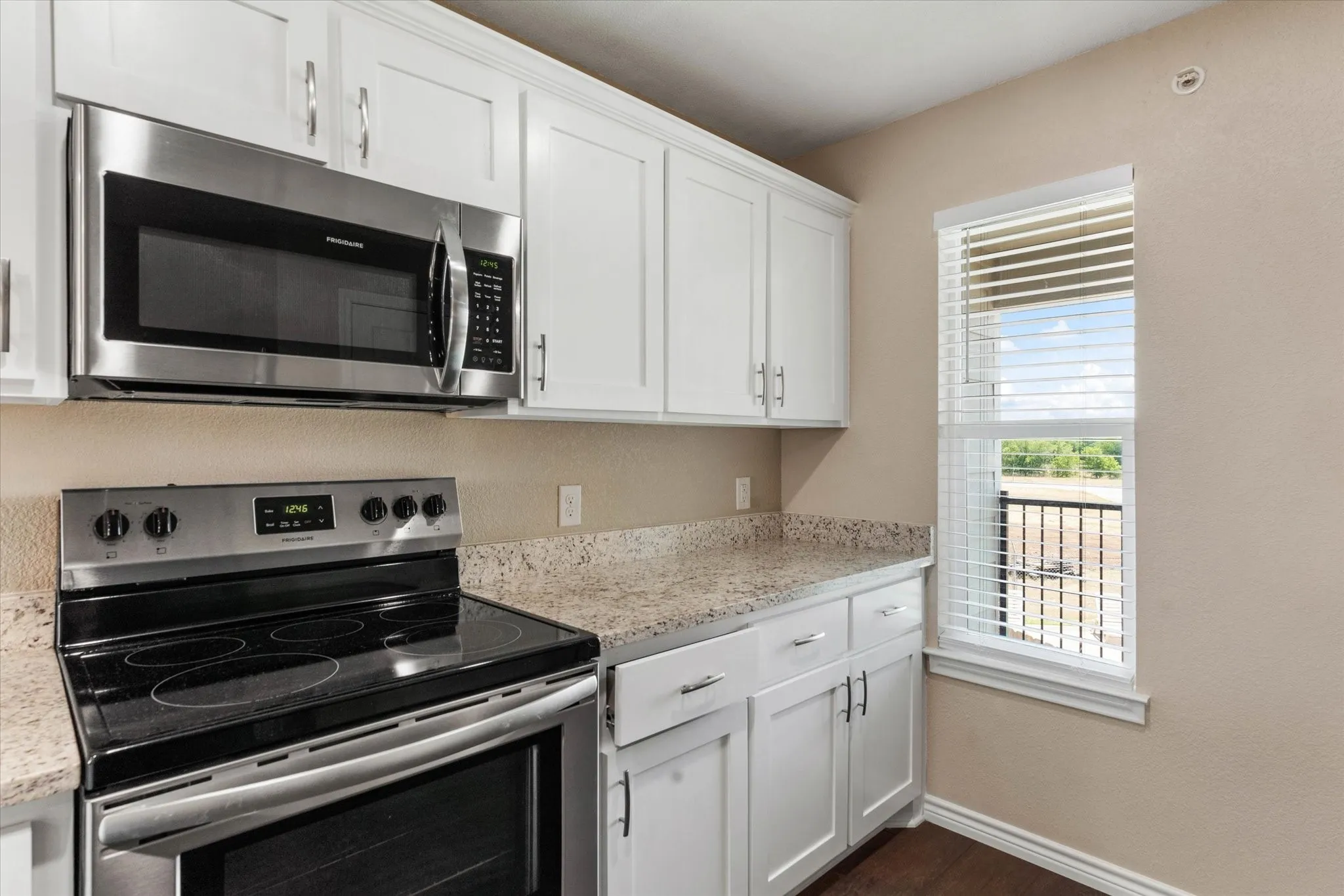 Kitchen featuring white cabinets, stainless steel appliances, light stone counters, and dark wood-type flooring