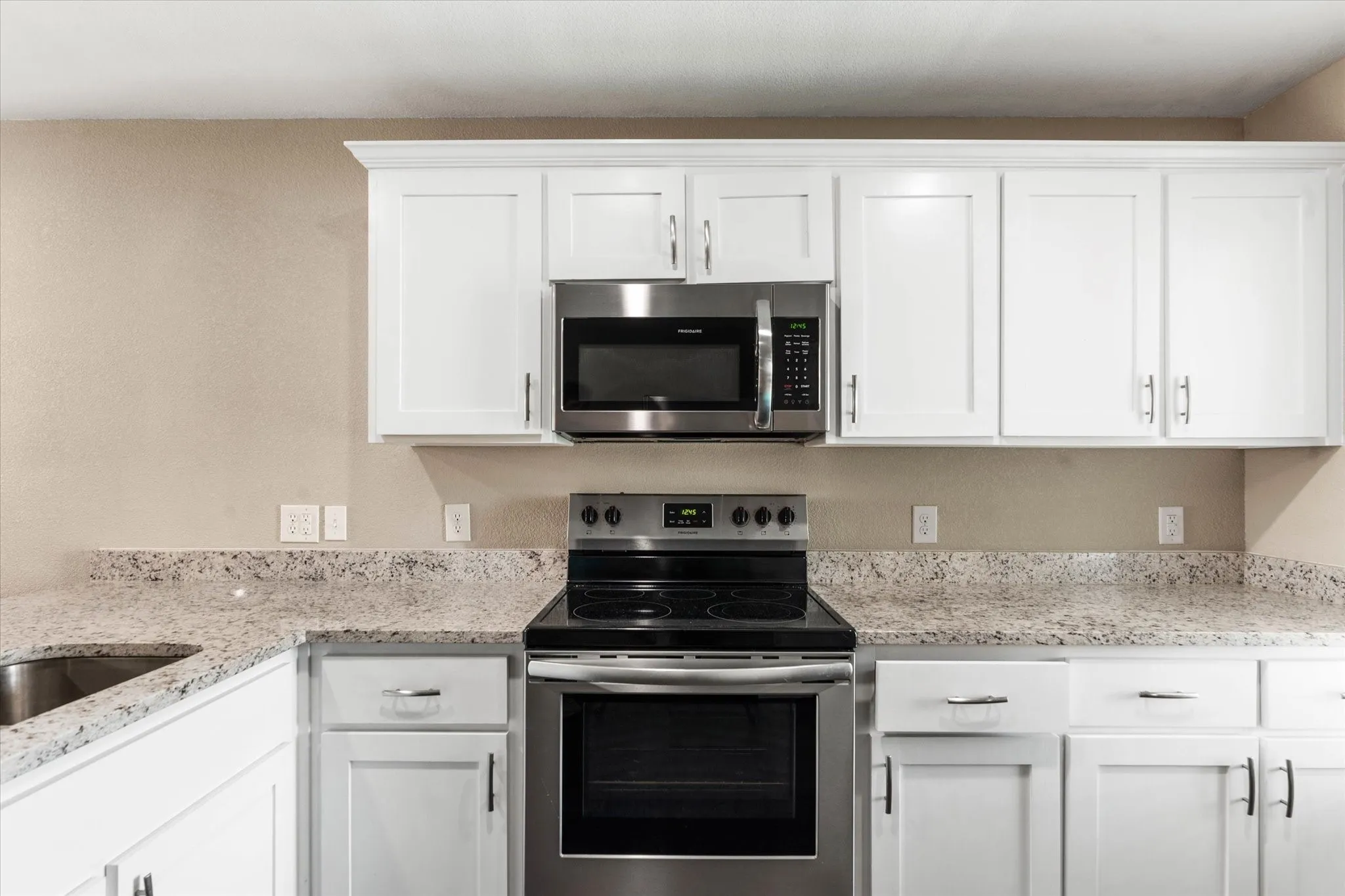 Kitchen with light stone countertops, white cabinets, and stainless steel appliances