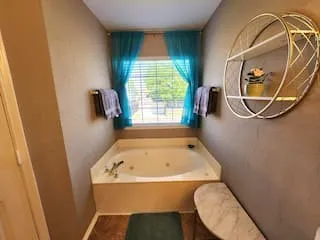 Corner soaking tub with a window, wood-finish flooring, and wall-mounted shelving