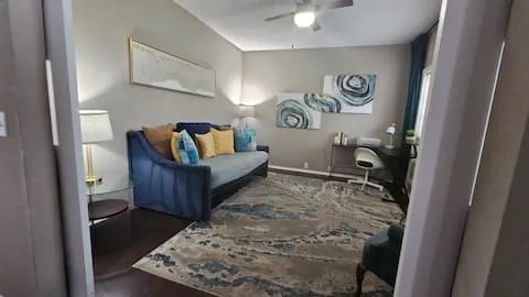 Dark wood-finish flooring, ceiling fan, and window with solid drapes