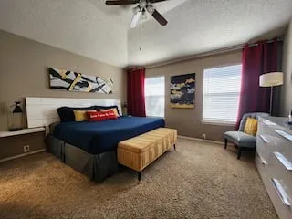 Vaulted ceiling with a ceiling fan, carpeted flooring, and multiple windows with blinds