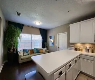 Spacious kitchen island with white countertop, white cabinetry with dark hardware, under-cabinet lighting, and dark wood-finish flooring