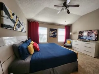 Vaulted ceiling with a ceiling fan, multiple windows with drapes, and carpeted flooring