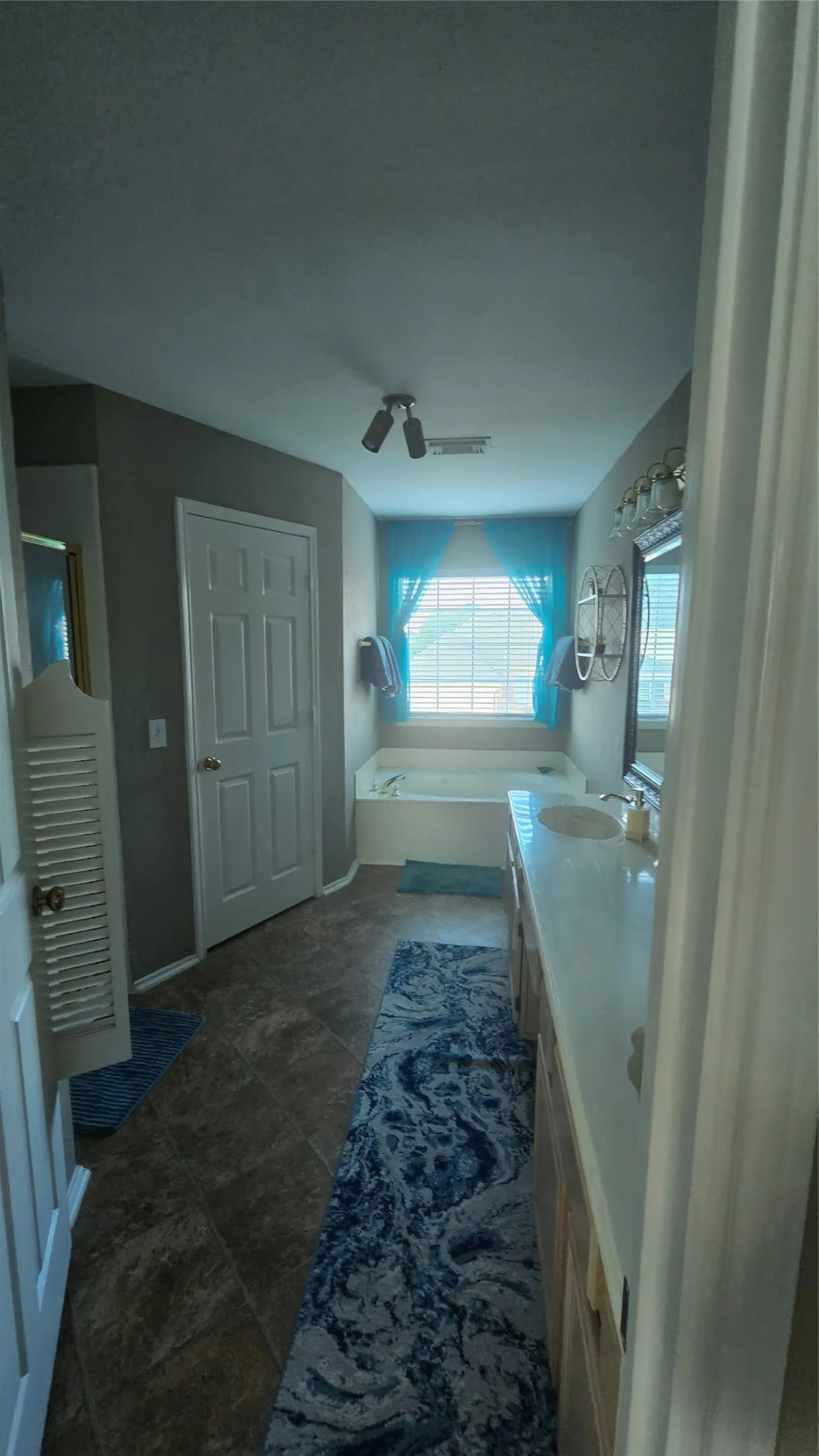 Dual vanity with integrated sinks, built-in soaking tub, tiled flooring, and window with blinds