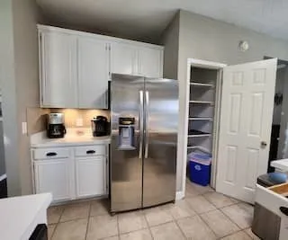 Kitchen featuring white cabinetry, stainless steel refrigerator, white countertops, tile flooring, and built-in pantry shelving
