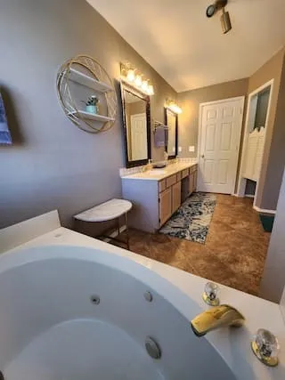 Jetted soaking tub, dual vanity with framed mirrors, built-in cabinetry, overhead track lighting, and wood-finish flooring