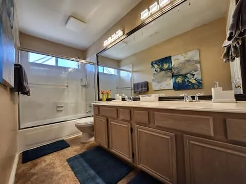 Dual vanity with integrated sinks, brushed nickel fixtures, wood-finish cabinetry, and a full-width mirror