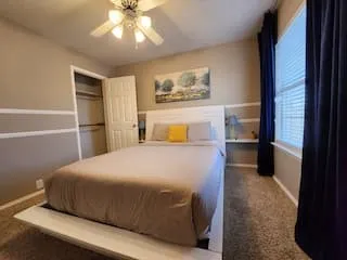 Built-in shelving, window with blinds, ceiling fan with light fixture, wall-to-wall carpeting, and a closet with bifold door