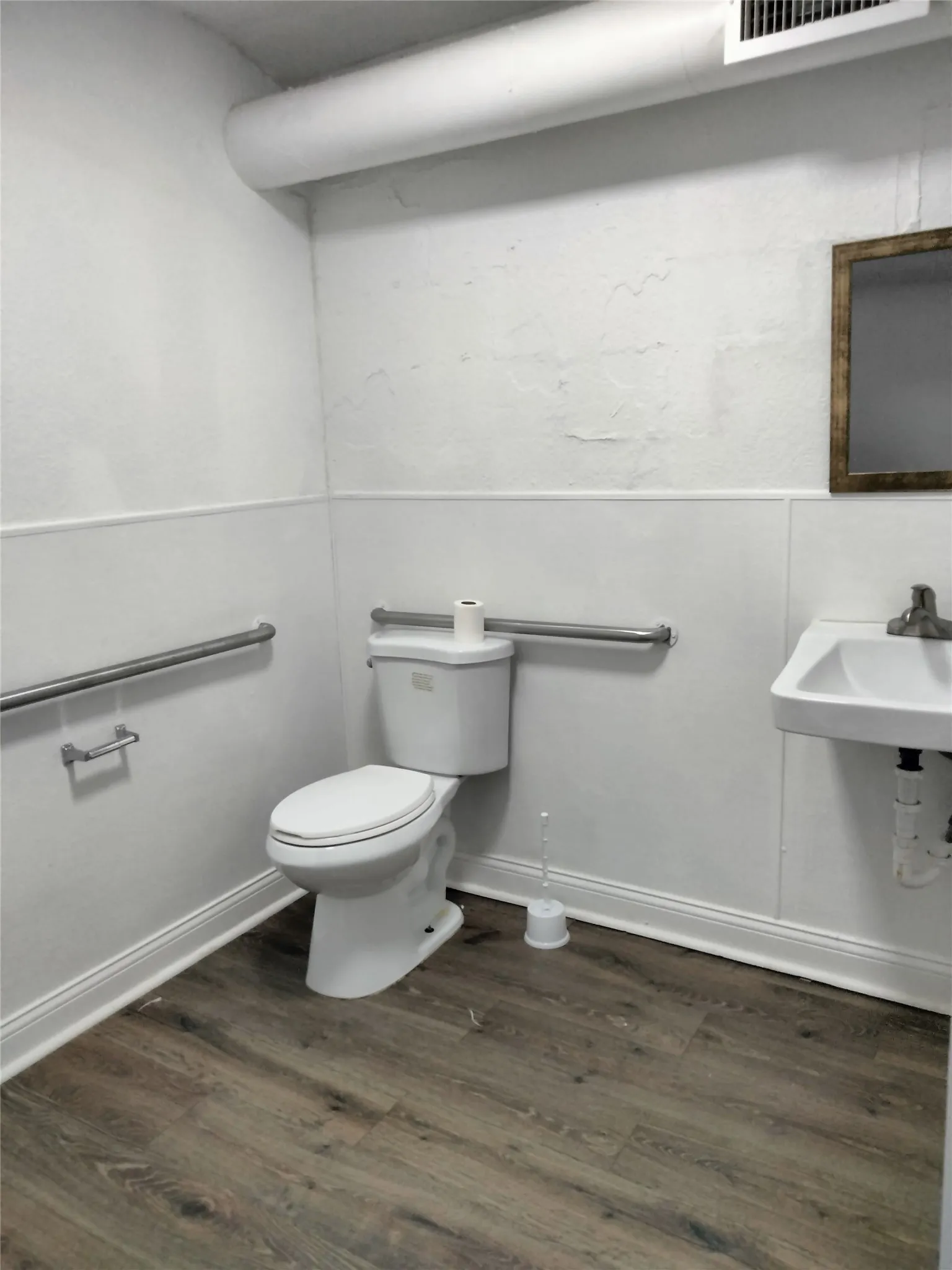 Wall-mounted sink with chrome faucet, wood-finish flooring, and white wainscoting