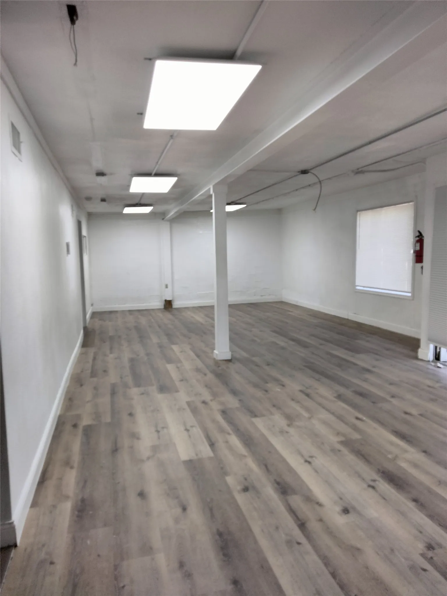 Spacious interior with wood-finish flooring, white walls, and multiple rectangular ceiling light fixtures