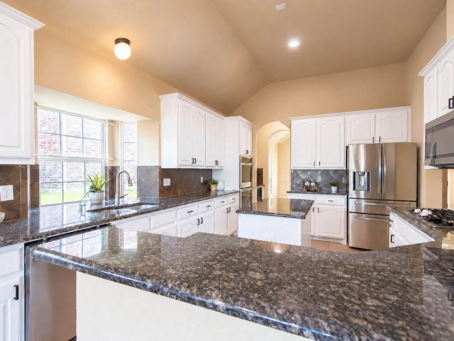 Kitchen featuring granite countertops, white cabinetry, stainless steel appliances, a center island, and a vaulted ceiling