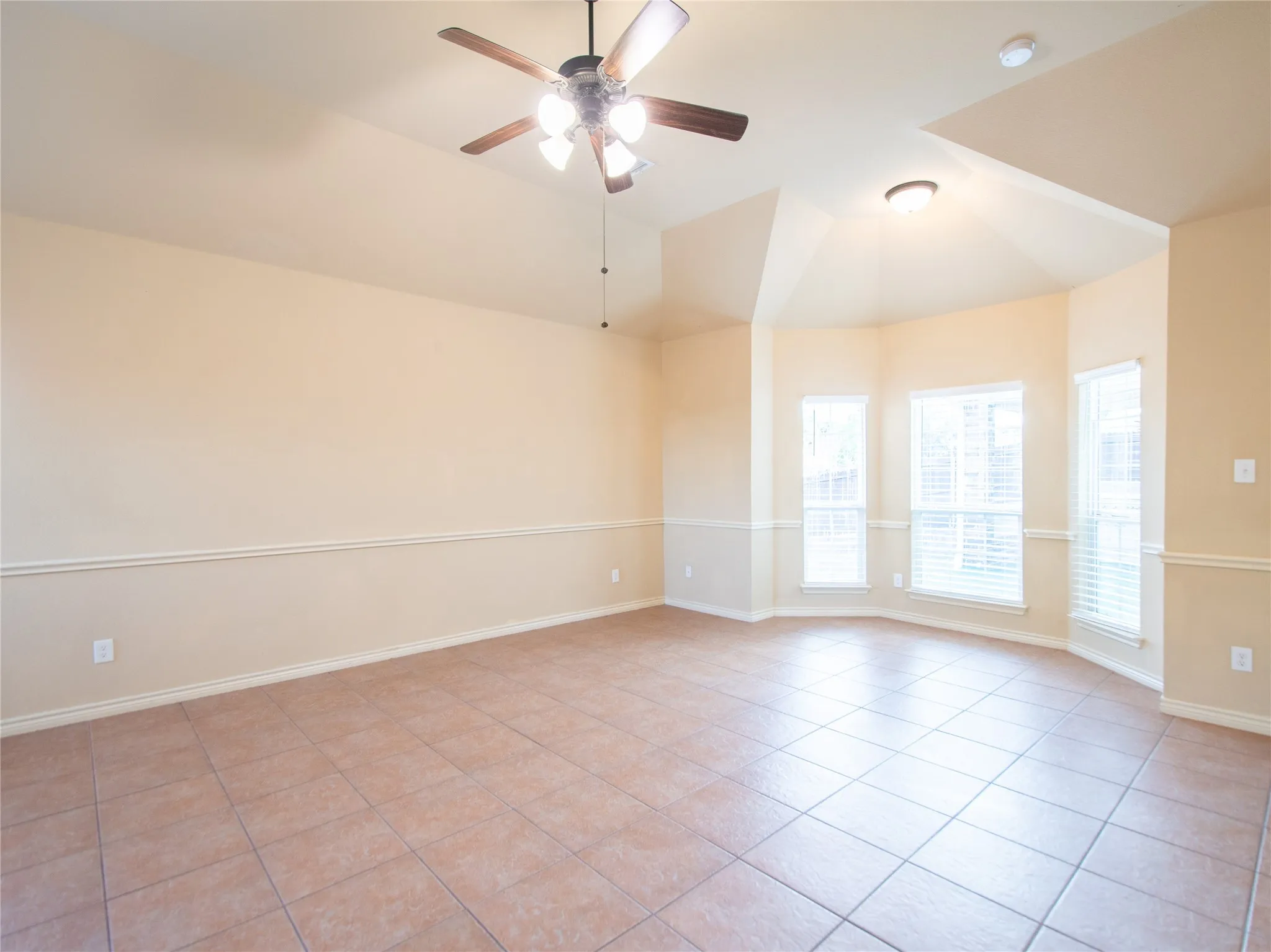 Vaulted ceiling with an attached ceiling fan, bay window with blinds, tile flooring, and decorative wall molding