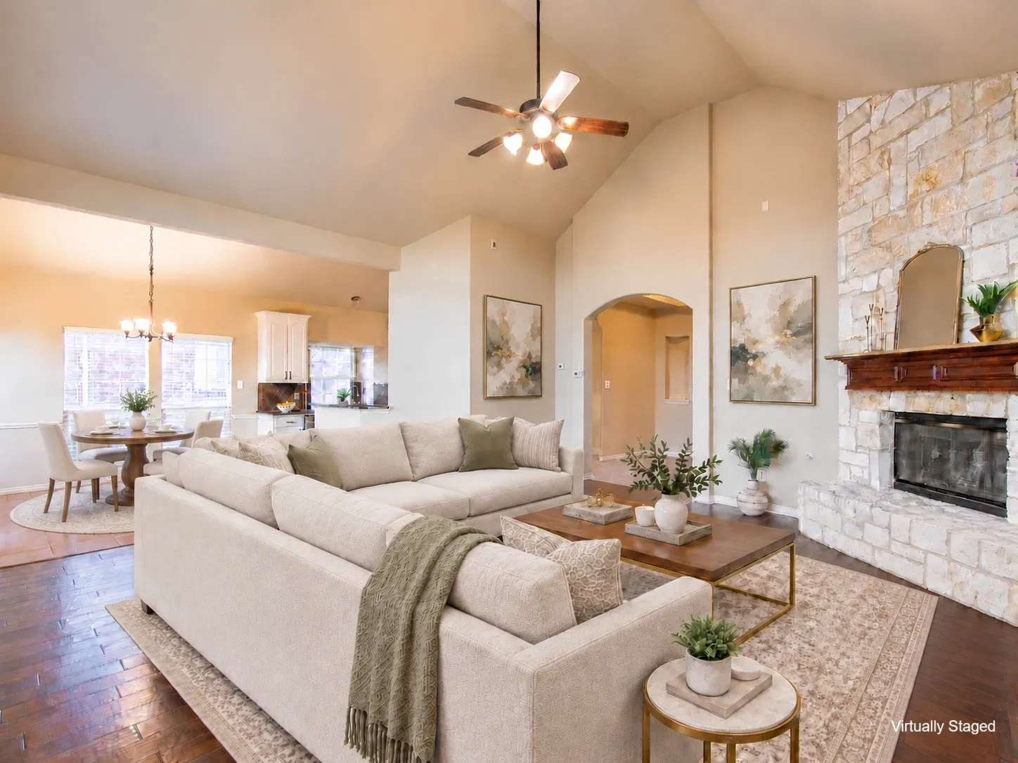 Vaulted ceilings, a stone-faced fireplace with a wood mantel, wood-finish flooring, a ceiling fan, and an arched doorway