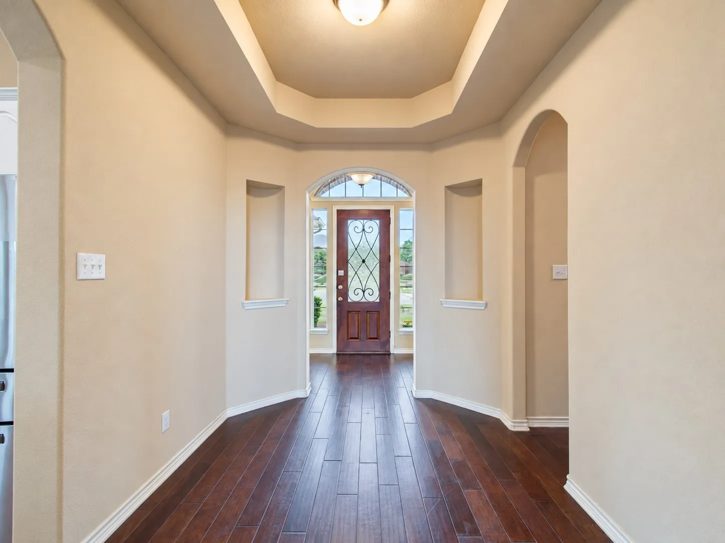 Tray ceiling, archways, wood-finish flooring, decorative entry door, recessed wall details