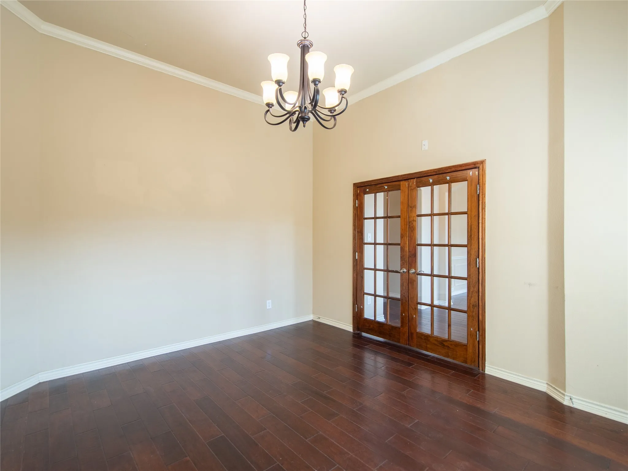 Vaulted ceiling with crown molding, dark wood-finish flooring, two-paneled glass French doors, and an iron chandelier