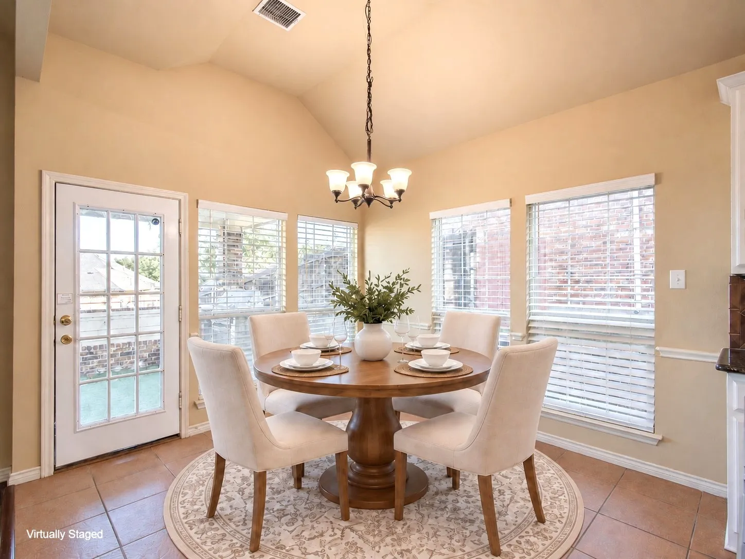 Vaulted ceiling, four windows with blinds, glass-paneled door, tile flooring, and a chandelier