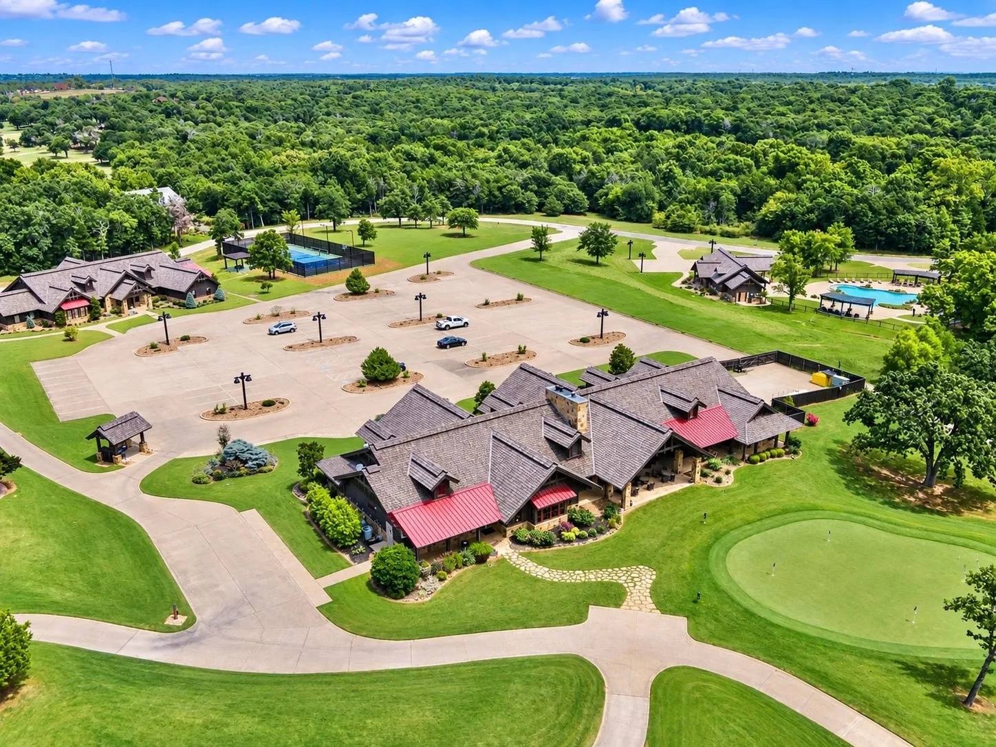 Clubhouse building with stone and wood siding, covered patio, golf course putting green, swimming pool area, and tennis courts