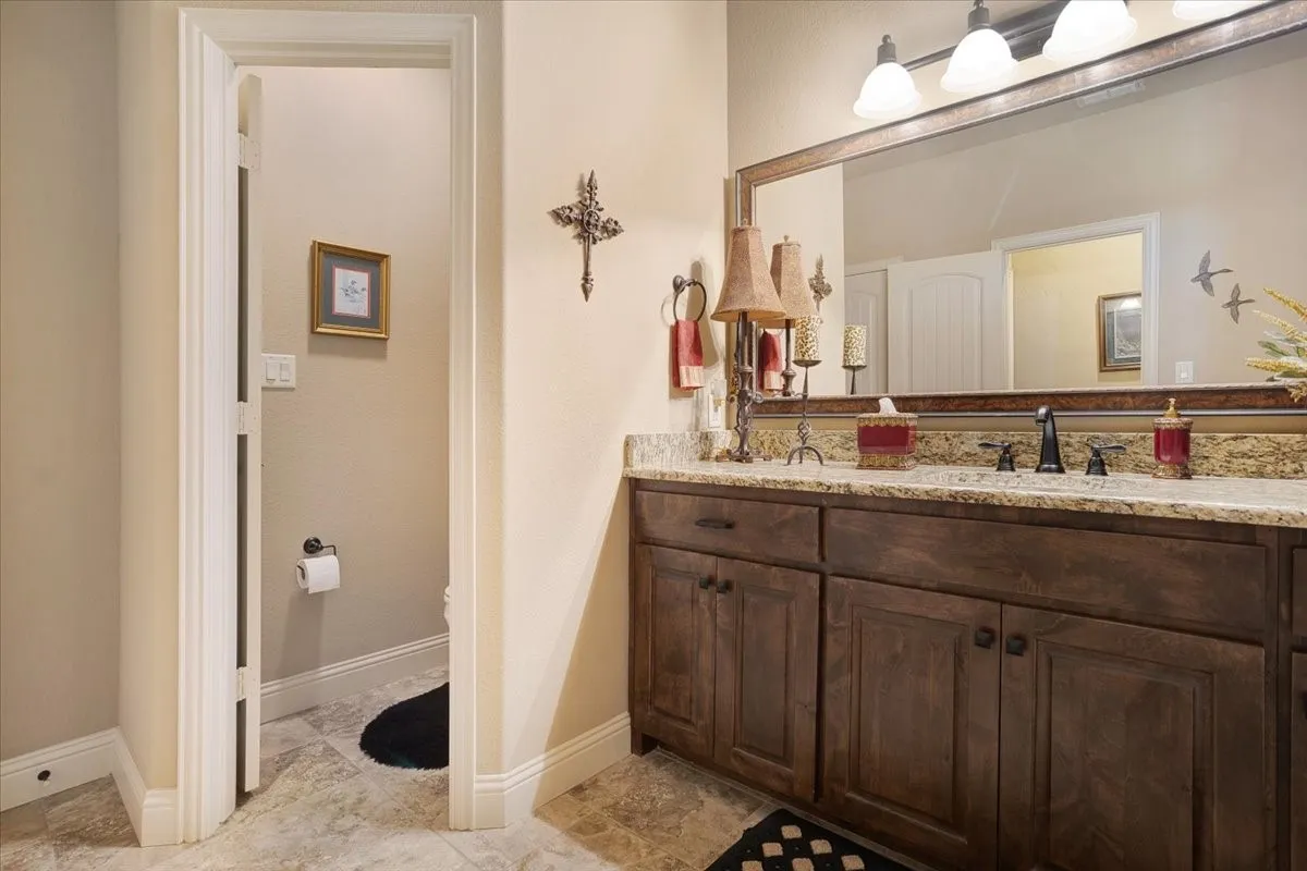 Wood-finish vanity with ample storage, a light-toned countertop, and a large wall-mounted mirror with overhead lighting