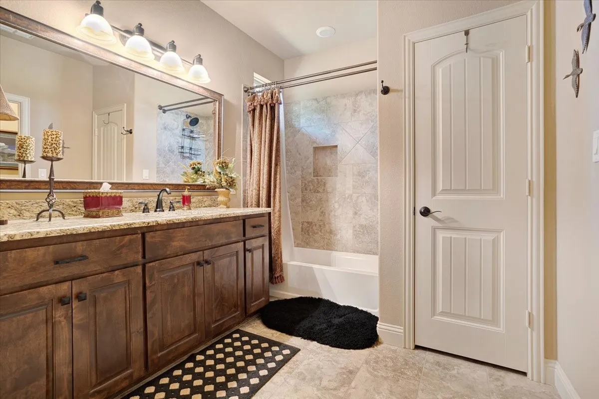 Wood-finish vanity with an integrated countertop, large vanity mirror, and a tiled shower/tub combination