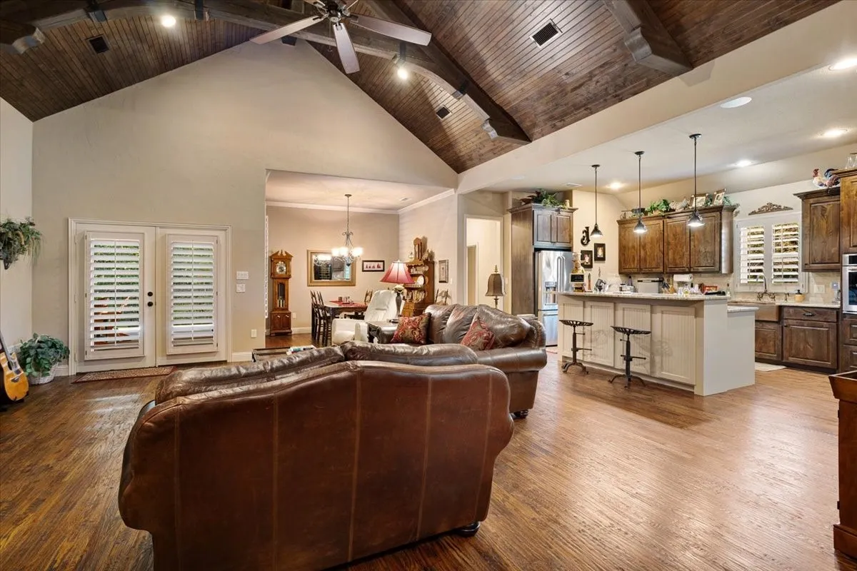 Vaulted wood-paneled ceiling, wood-finish flooring, kitchen island with seating, pendant lighting, and double glass doors with plantation shutters