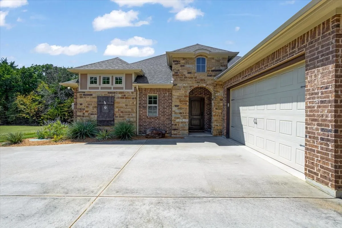 Brick and stone exterior with an arched entryway, multiple windows, and an attached garage
