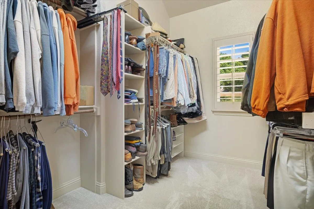 Walk-in closet with custom shelving, multiple hanging rods, built-in shoe storage, and a window with white plantation shutters