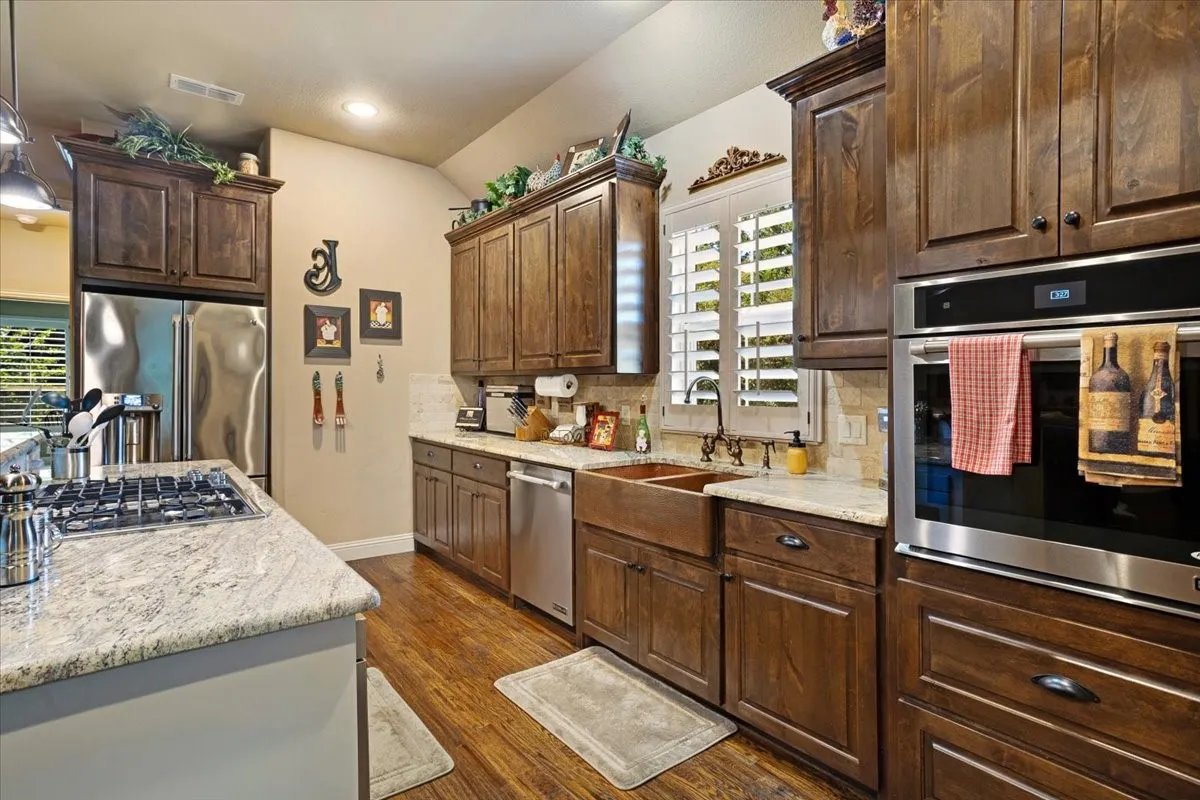Kitchen featuring wood-finish flooring, dark wood cabinetry, granite countertops, and stainless steel appliances