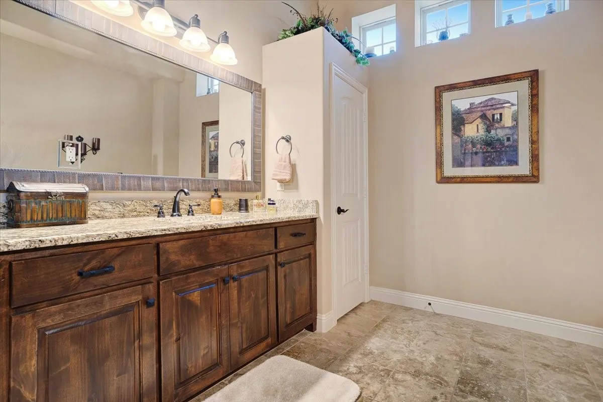Wood-finish cabinetry with a stone countertop, an expansive framed mirror, and upper transom windows