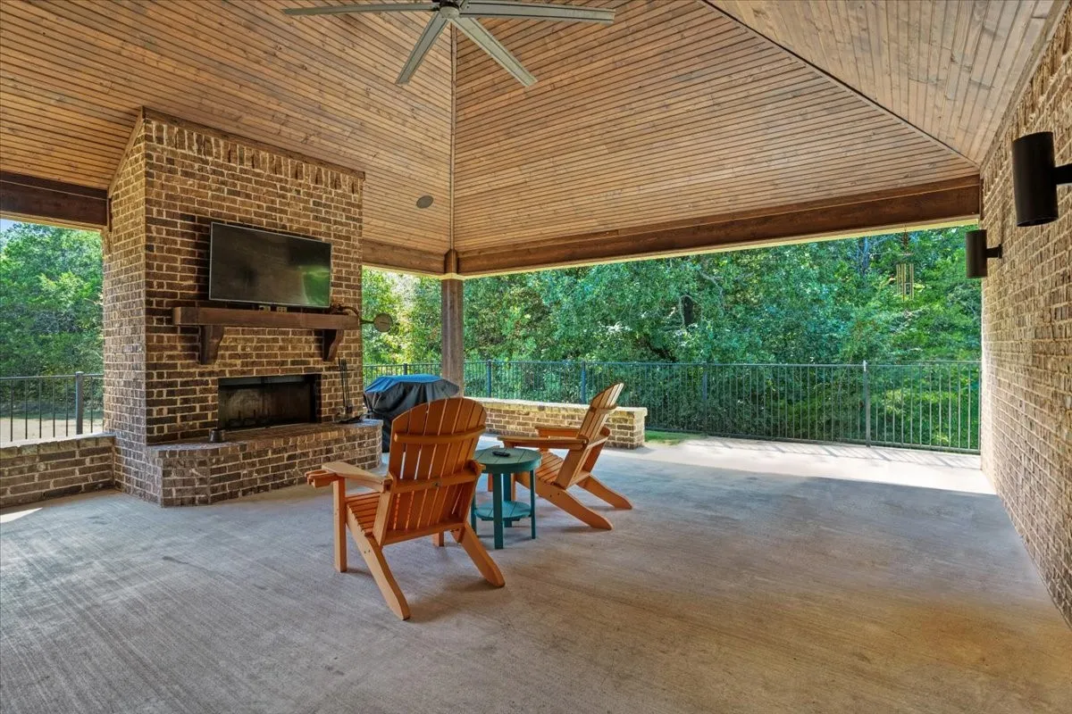 22x24 Covered outdoor patio featuring a brick fireplace, wood-plank ceiling, and concrete flooring