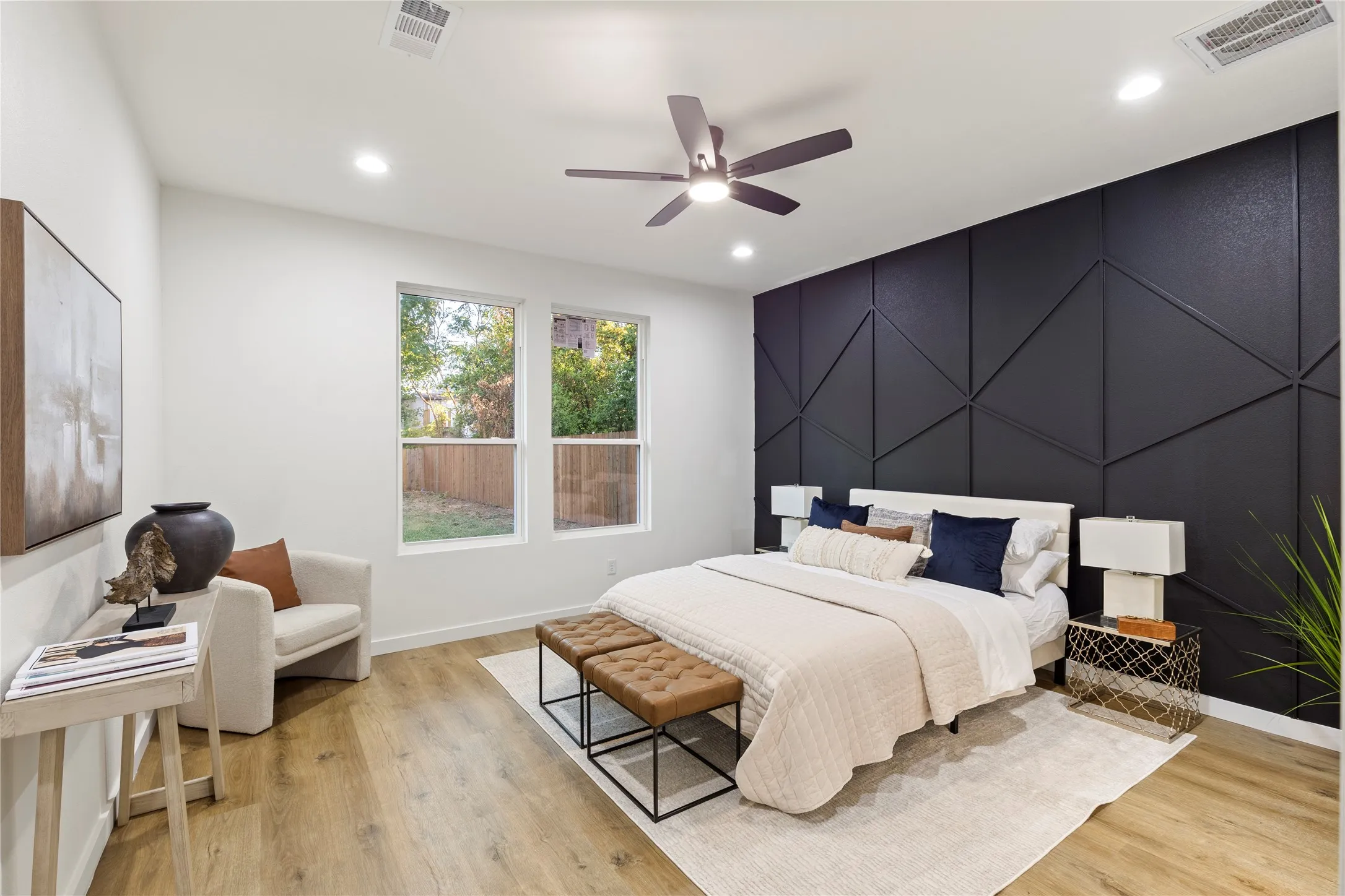 Accent wall with geometric paneling, wood-finish flooring, two large windows, recessed lighting, and a ceiling fan