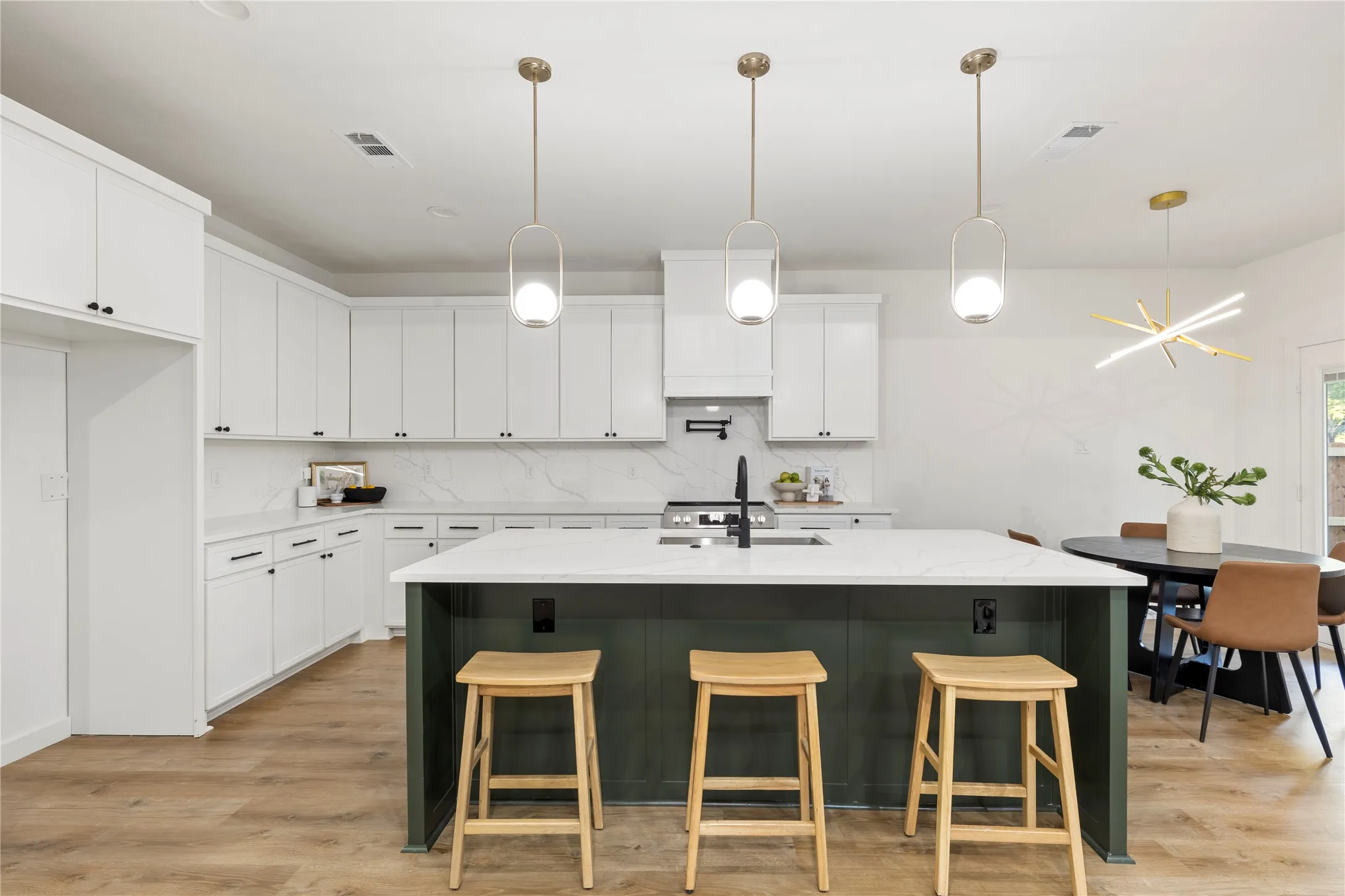 White shaker cabinetry, light-toned wood-finish flooring, a kitchen island with a contrasting finish, an undermount sink, and stylish pendant lighting